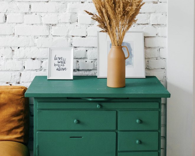 Green dresser with decorations against a white brick wall.